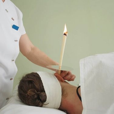 Image of the back of a head with therapist holding a lit ear candle in the ear.